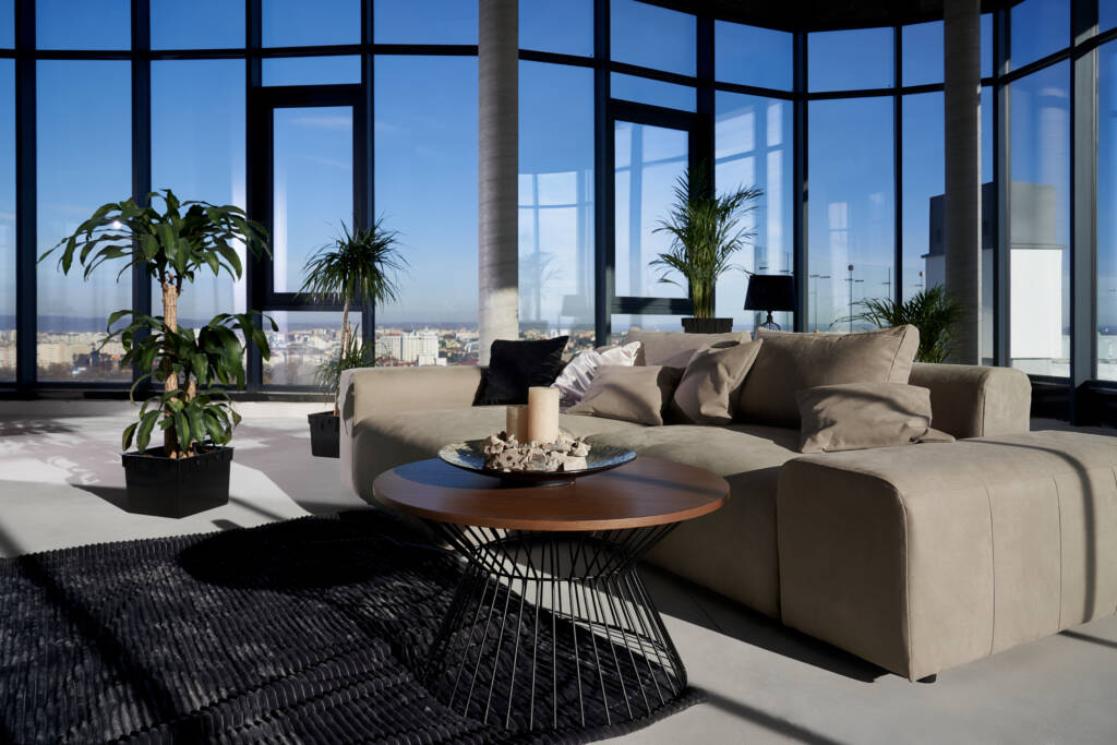 Interior moderno y luminoso con grandes ventanales de PVC de alto rendimiento, sillón beige y alfombra oscura, destacando el aislamiento térmico y acústico superior de los sistemas TermProtect con 10 años de garantía.