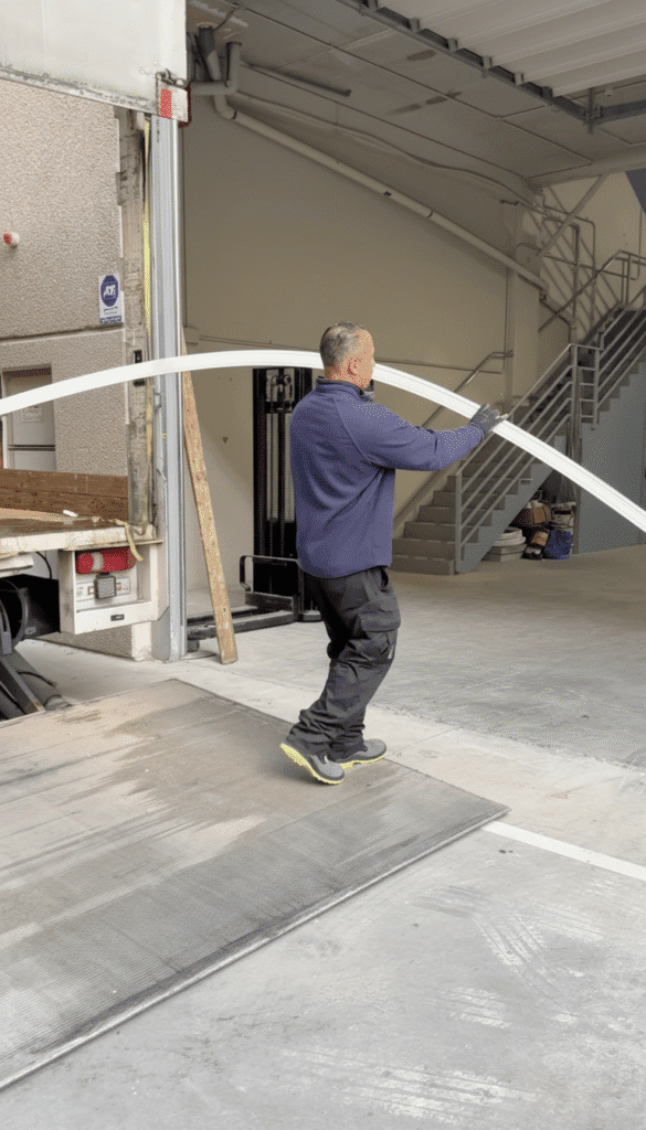 Hombre en muelle de carga moviendo arco estructural blanco, logística de almacén.